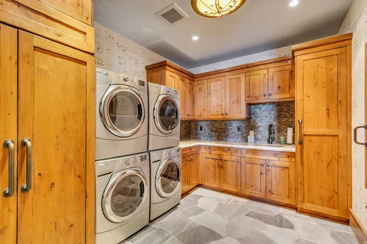 Dedicated utility room featuring two sets of stacked laundry appliances, extensive wood cabinetry, and a countertop with an integrated sink