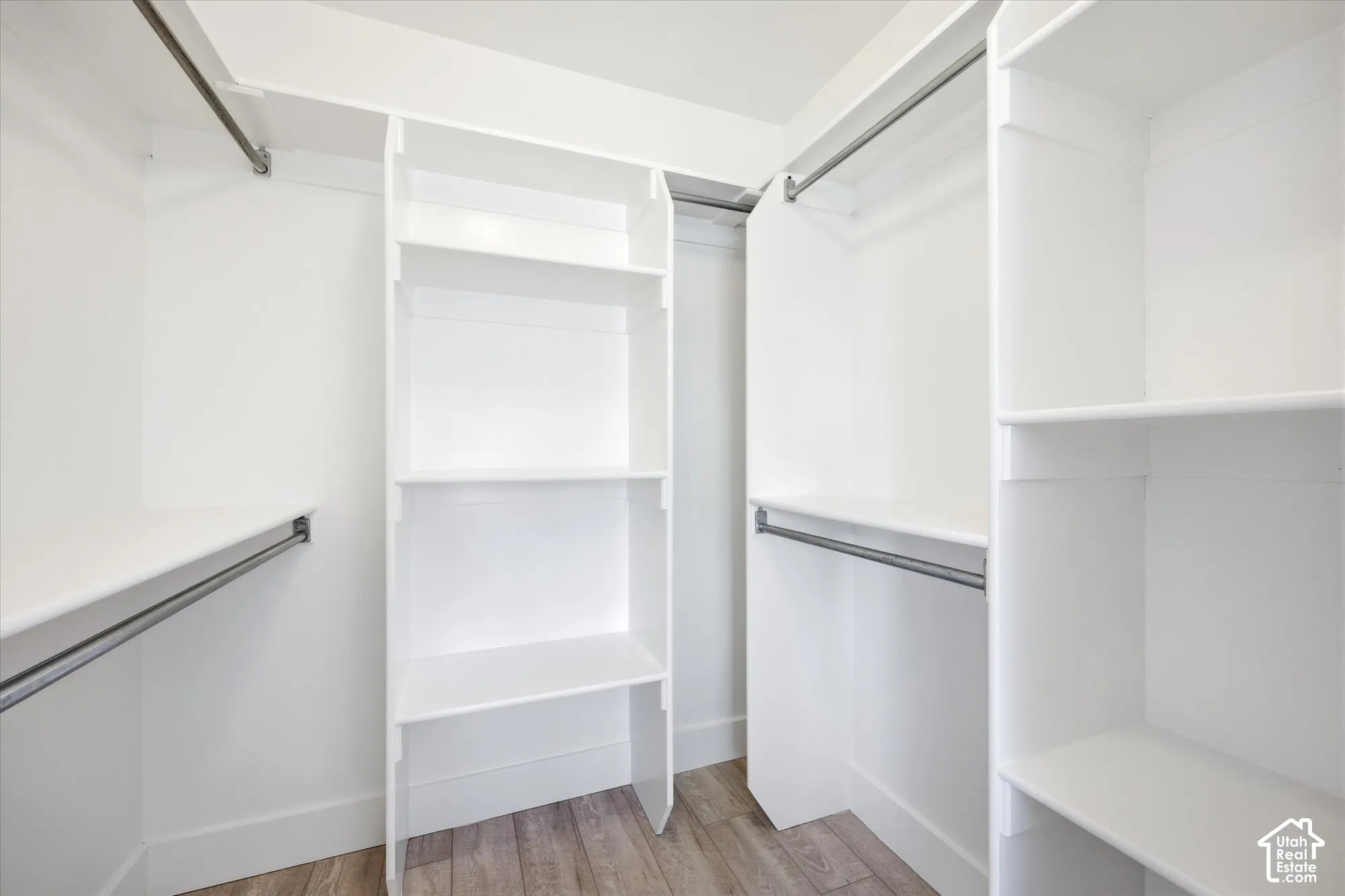Walk-in closet featuring white built-in shelving, multiple hanging rods, and wood-finish flooring