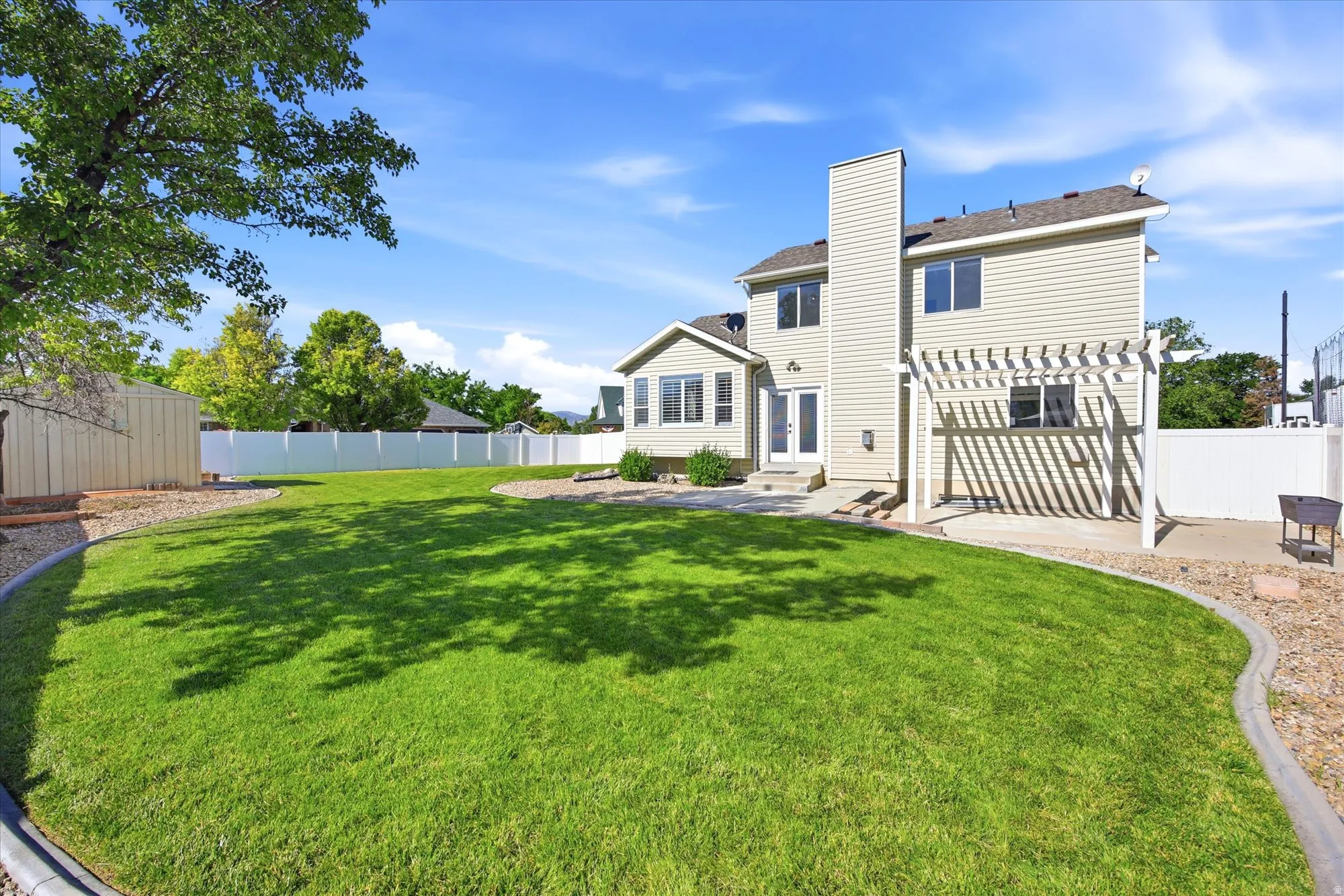 Expansive fenced backyard featuring a substantial lawn, paved patio with a pergola, and a sunroom with exterior access