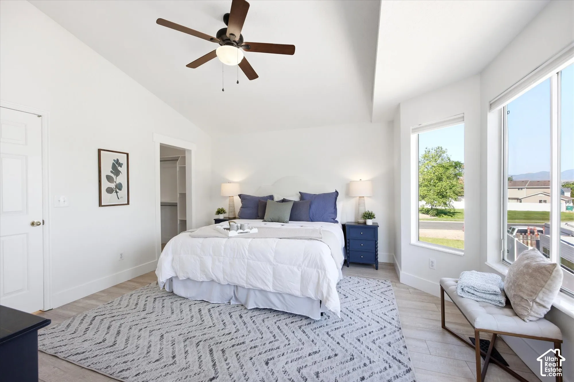 Spacious room featuring vaulted ceilings, wood-finish flooring, a contemporary ceiling fan, and large windows providing ample natural light