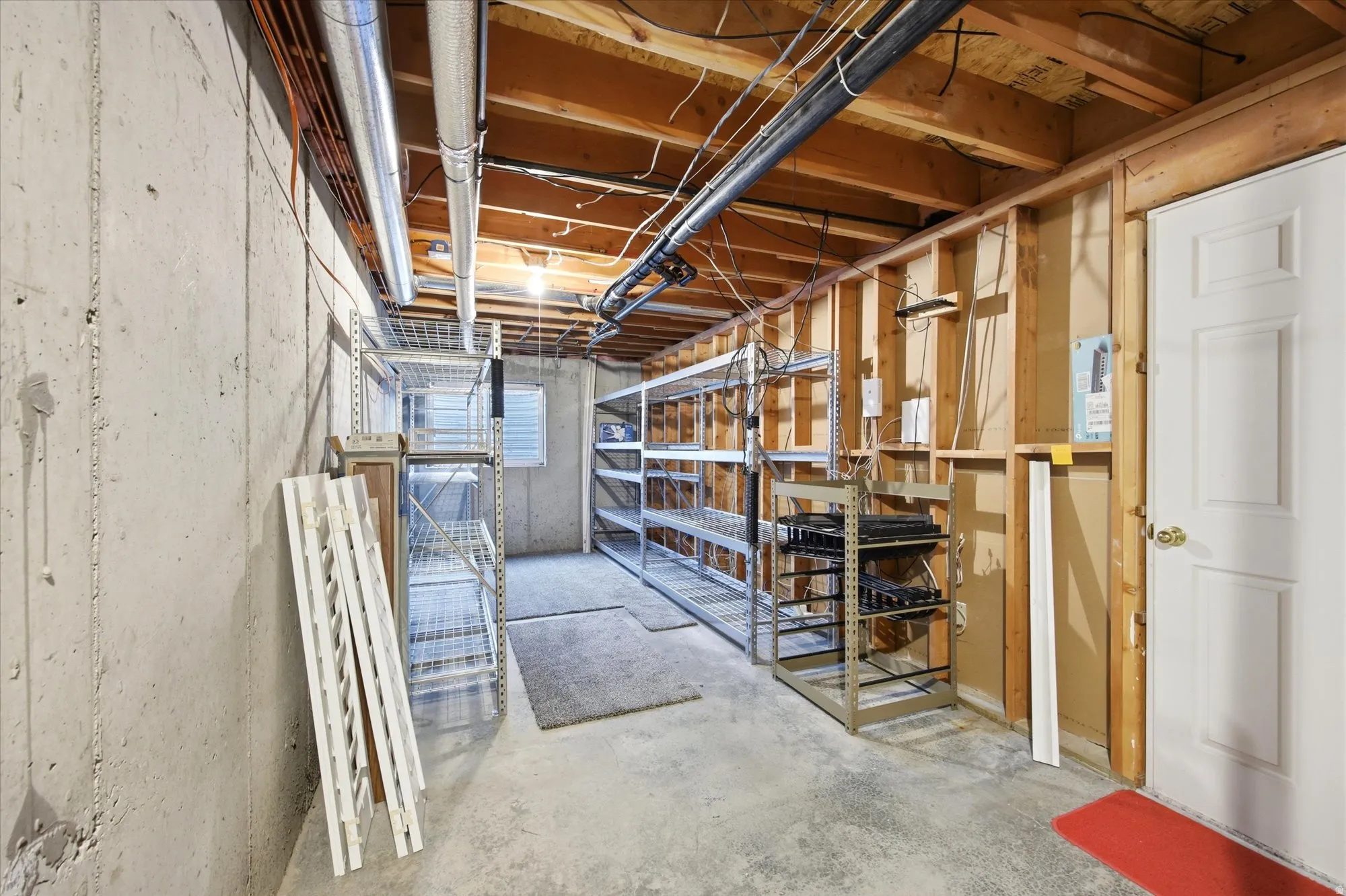 Unfinished basement offering exposed concrete walls, concrete flooring, exposed ceiling joists, and a paneled white door