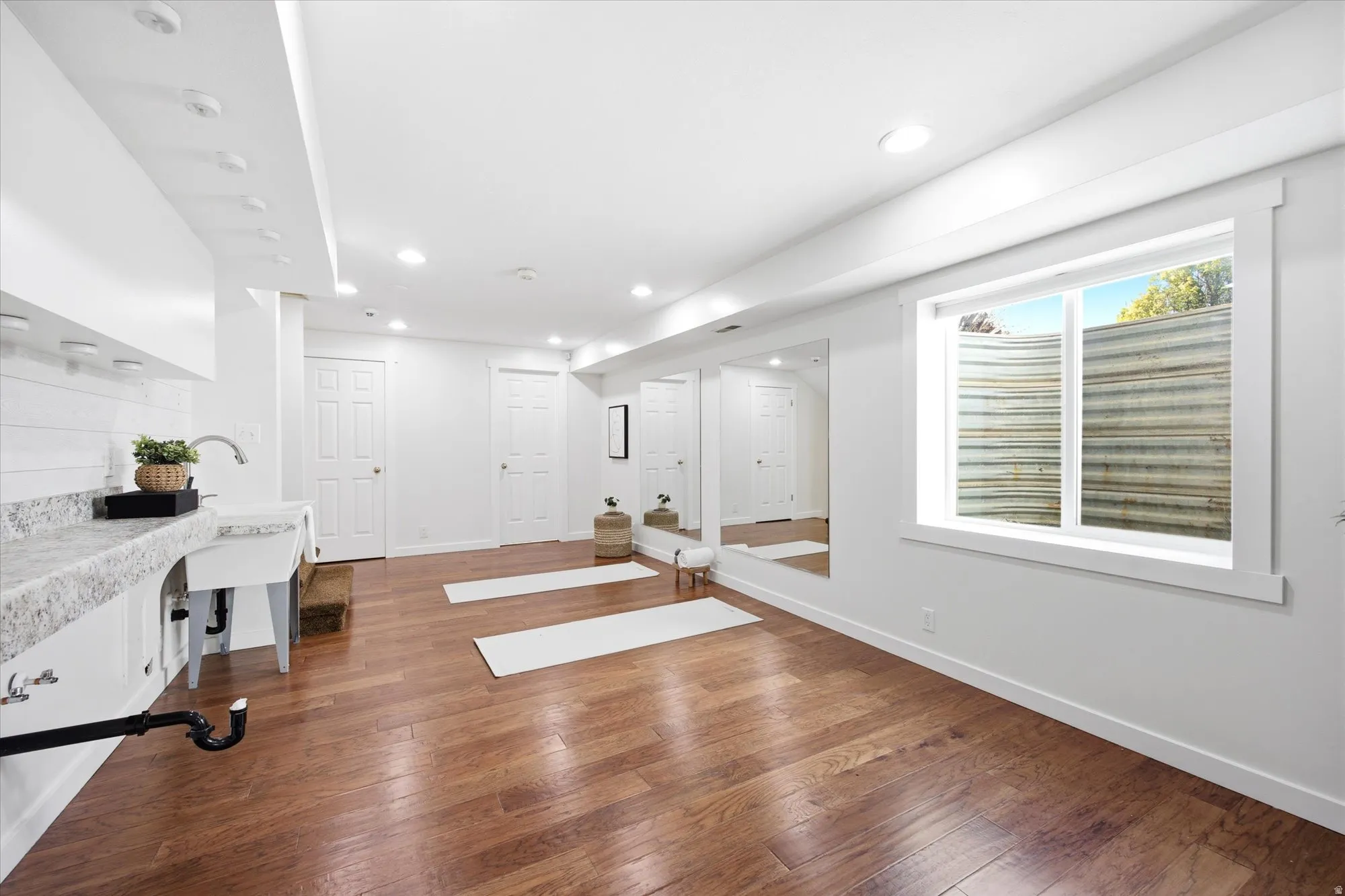 Finished basement space featuring wood-finish flooring, recessed lighting, and a utility sink with a stone-finish countertop