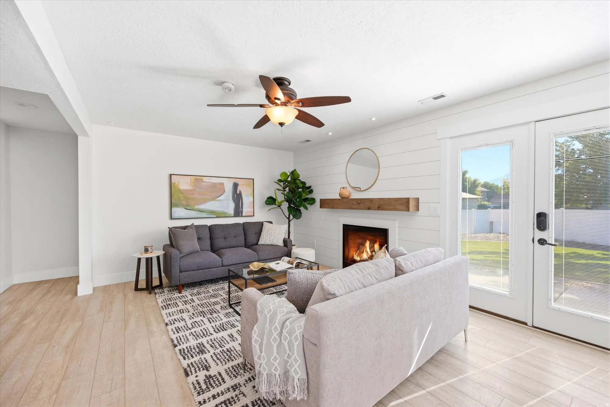 Living area featuring wood-finish flooring, a ceiling fan with integrated lighting, and a white shiplap-style accent wall
