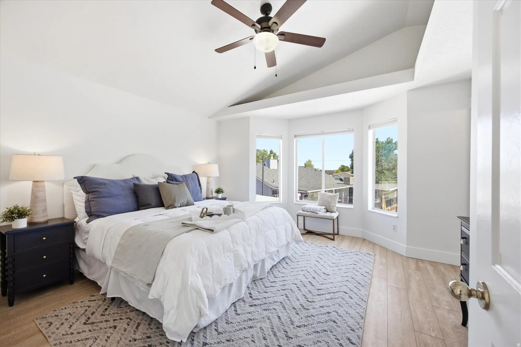 Vaulted ceilings enhance this room featuring wood-finish flooring, a contemporary ceiling fan, and a bay window area