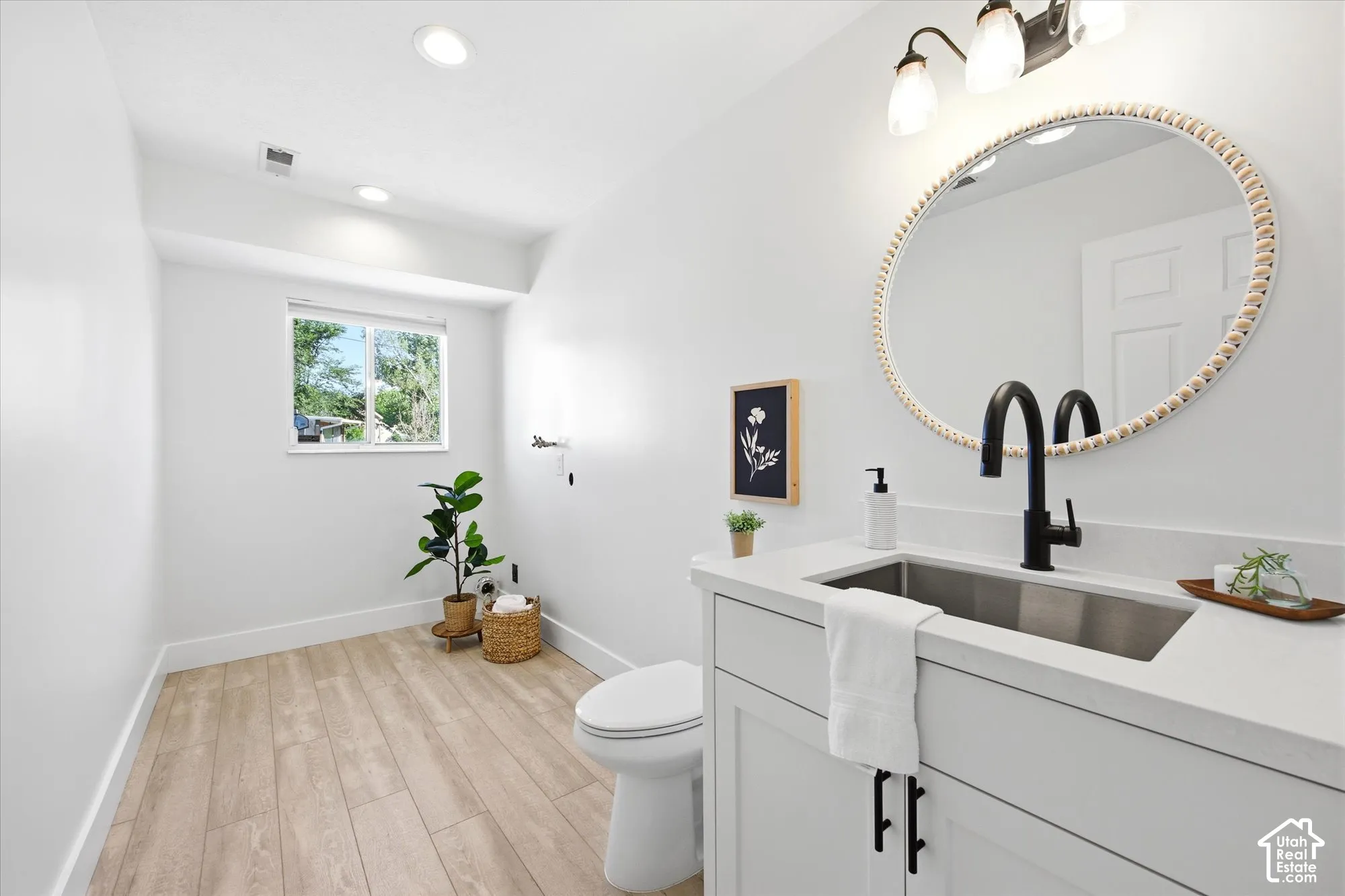 Contemporary bathroom featuring a white vanity with a stainless steel undermount sink, a matte black faucet, and a round decorative mirror