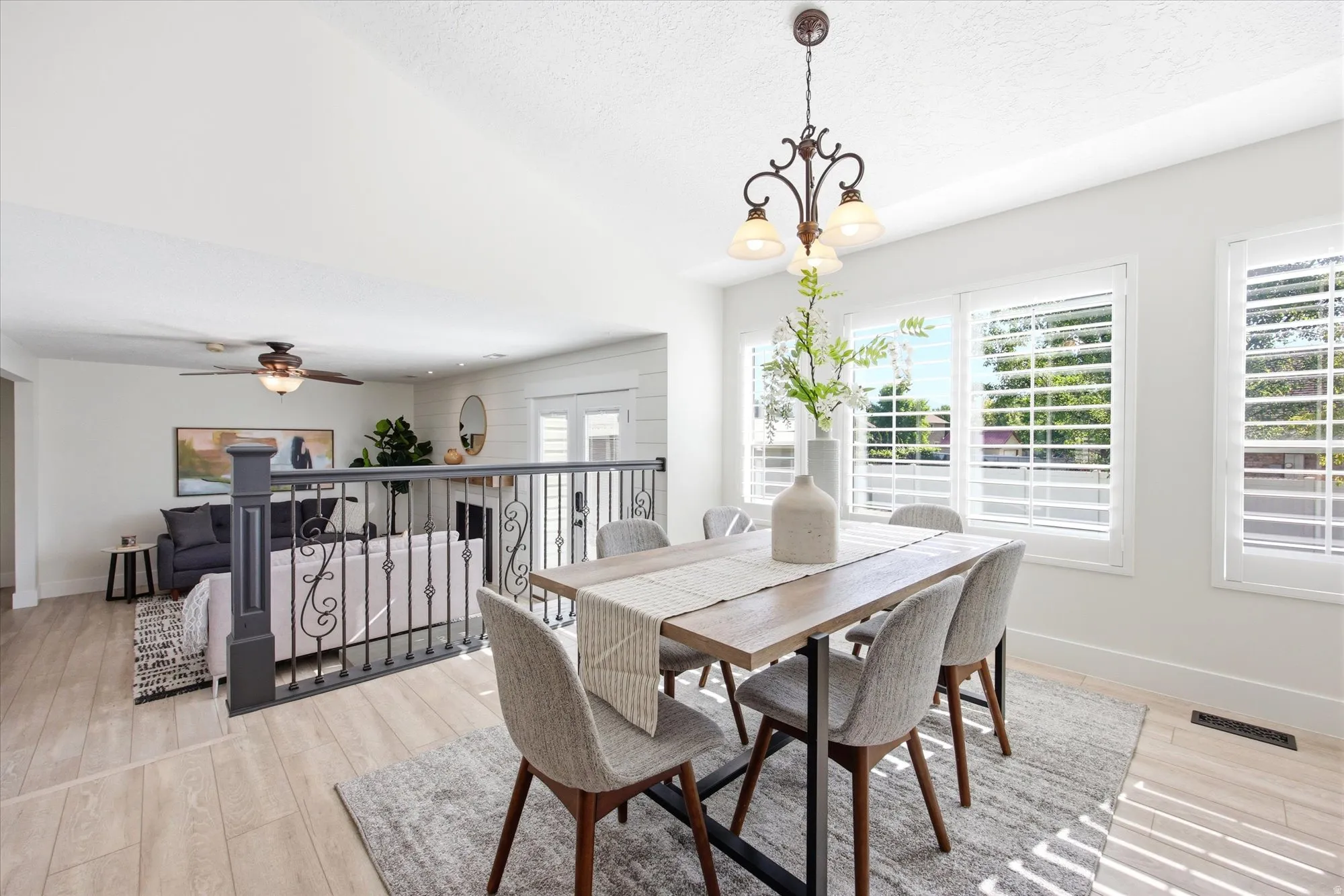 Bright dining area featuring a bronze-finish chandelier, three windows with white plantation shutters, and wood-finish flooring