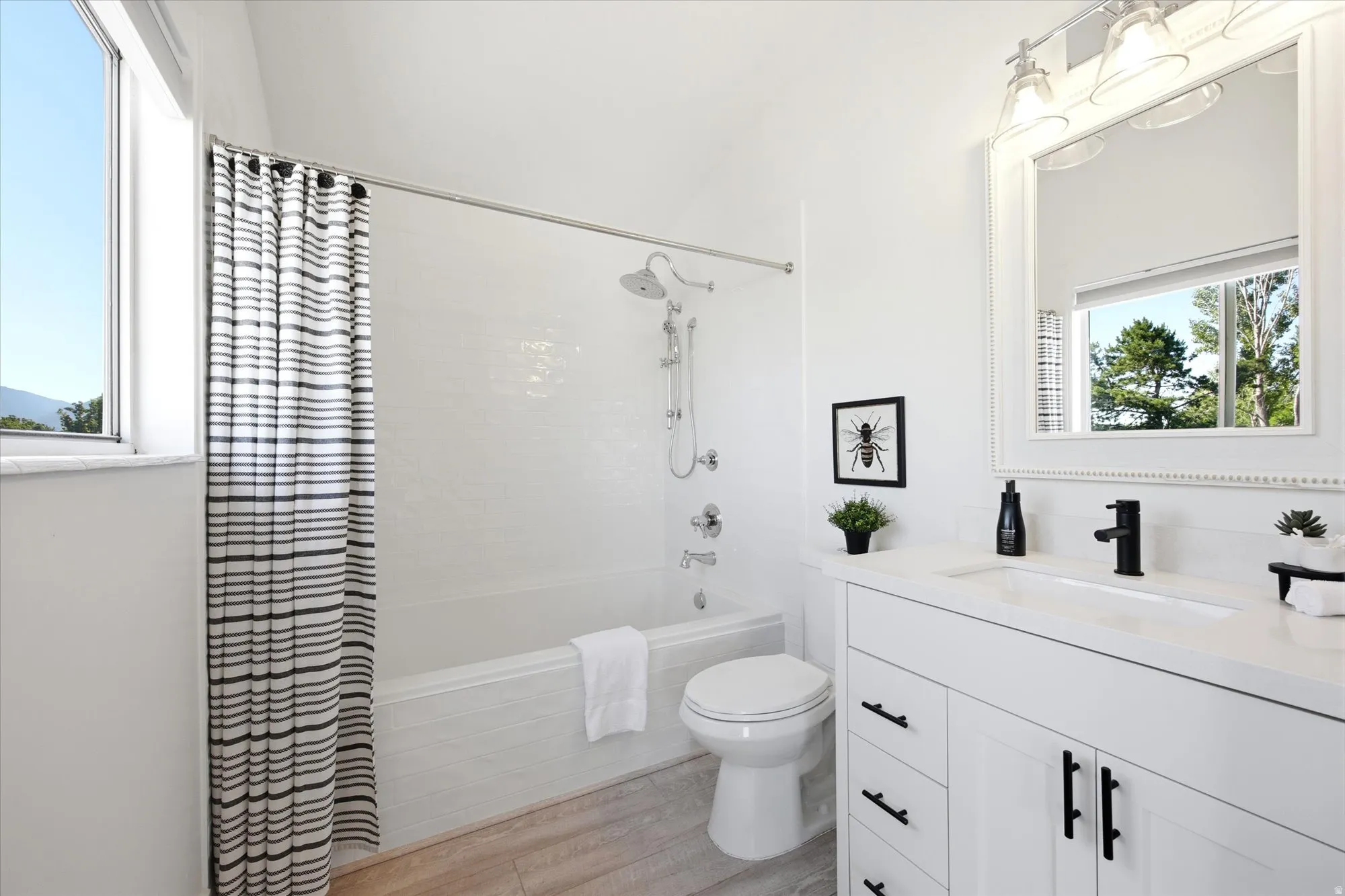 Bright bathroom featuring a white vanity with an integrated sink, a dark faucet, and a large mirror
