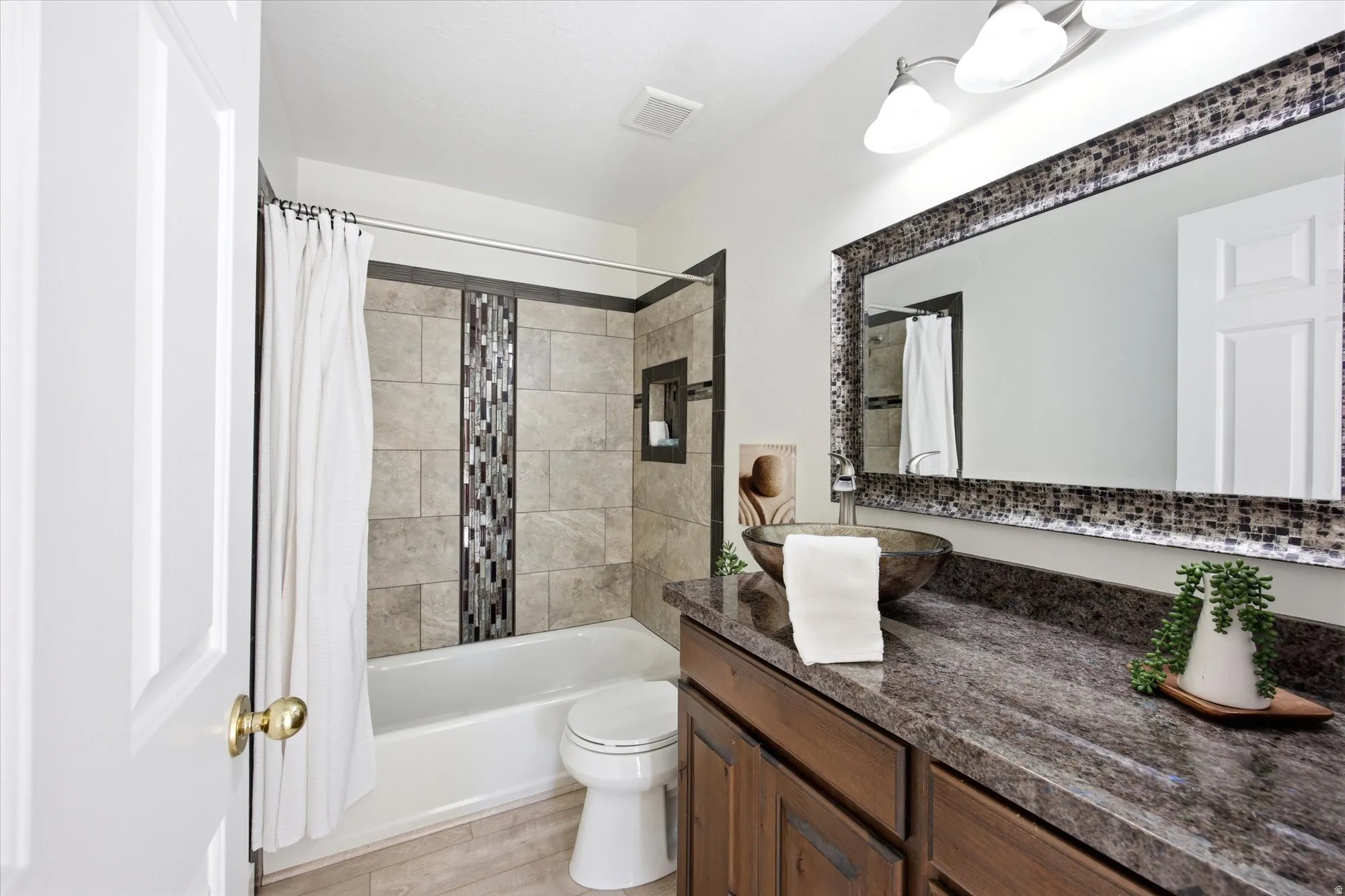 Bathroom featuring a tub/shower combination with mosaic tile accent, dark wood-finish vanity with stone-finish countertop, and vessel sink