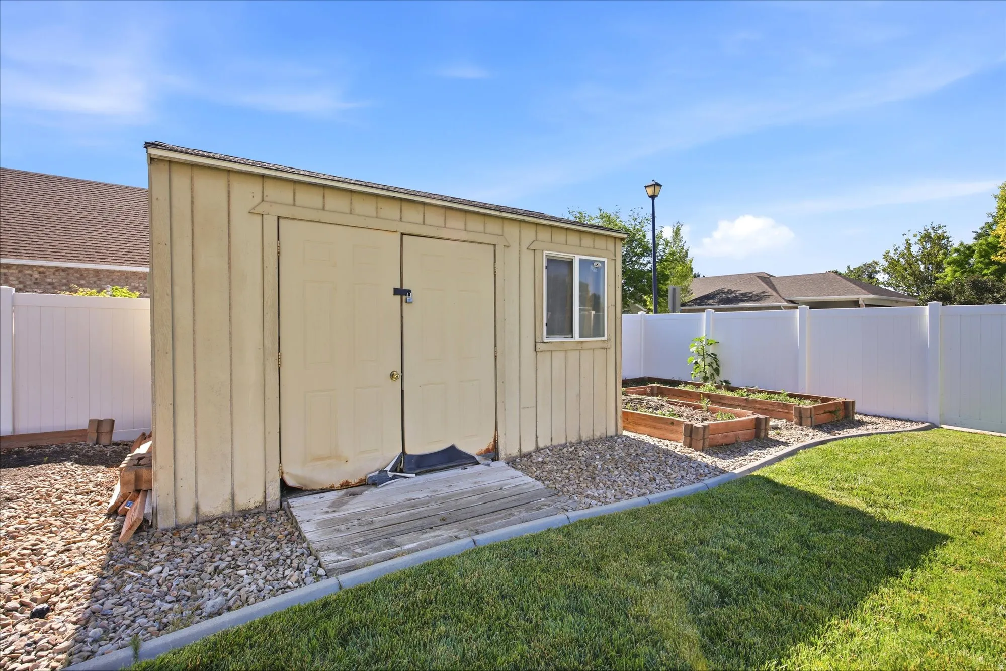 Backyard featuring a detached shed, raised garden beds, and a white privacy fence