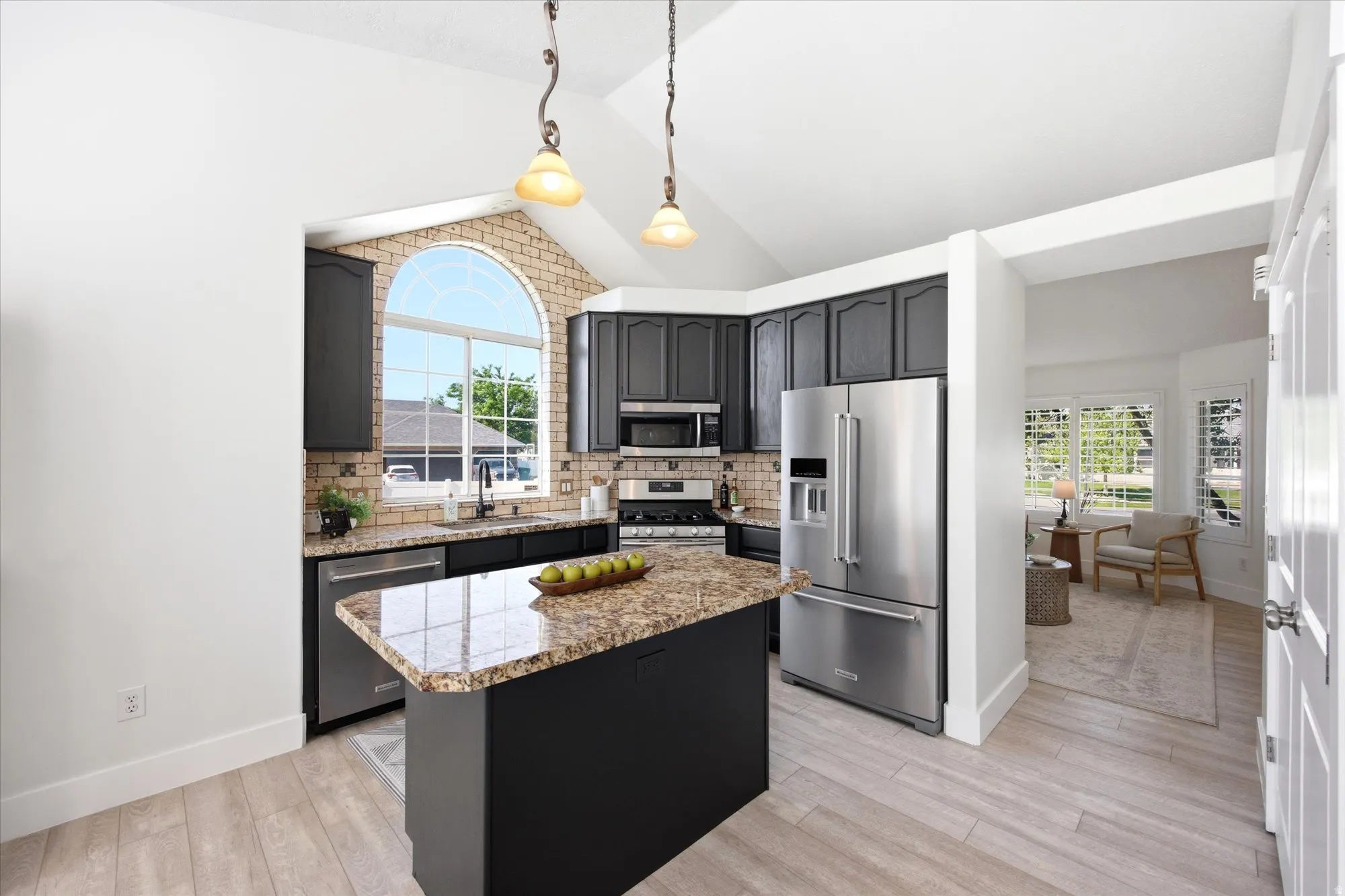 Kitchen featuring a vaulted ceiling, dark cabinetry, stainless steel appliances, and wood-finish flooring