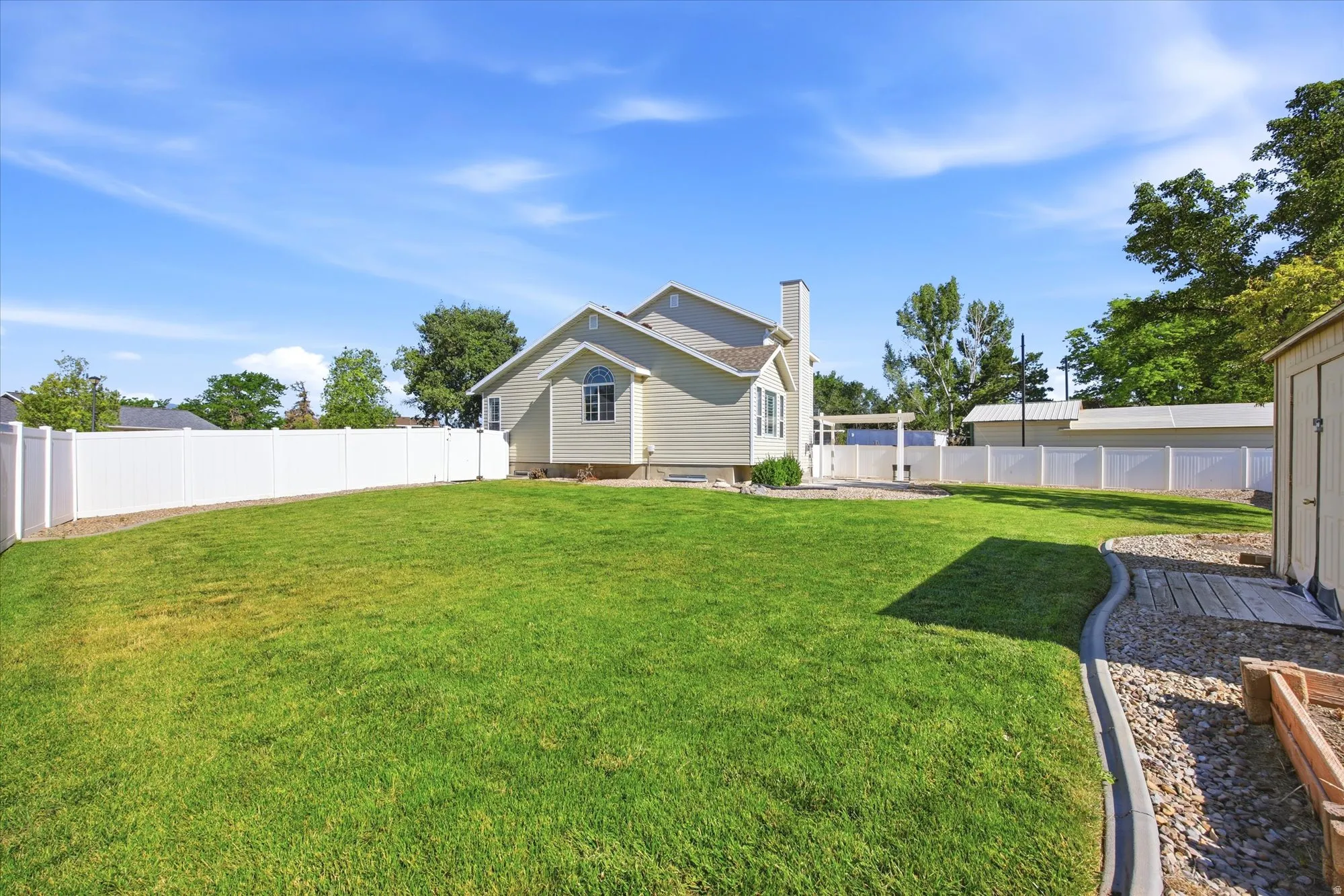 Expansive backyard featuring a lush lawn, white vinyl fencing, a gravel pathway with concrete edging, and a separate storage shed