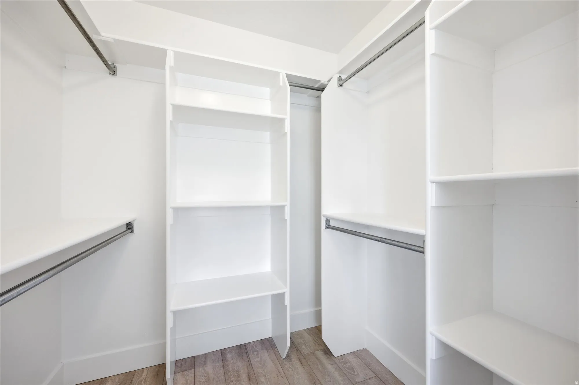 Walk-in closet featuring white built-in shelving, multiple hanging rods, and wood-finish flooring