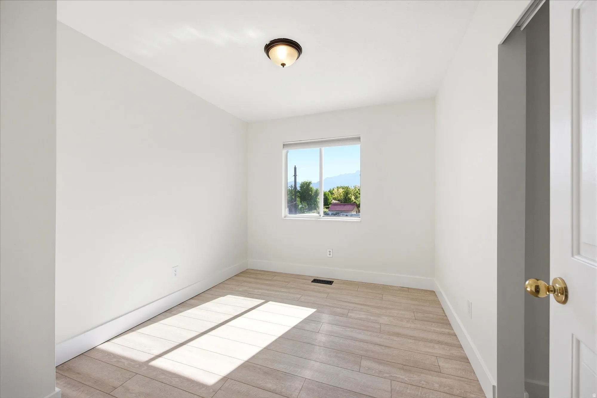 Neutral toned room featuring a single window, a ceiling-mounted light fixture, wood-finish flooring, and white trim
