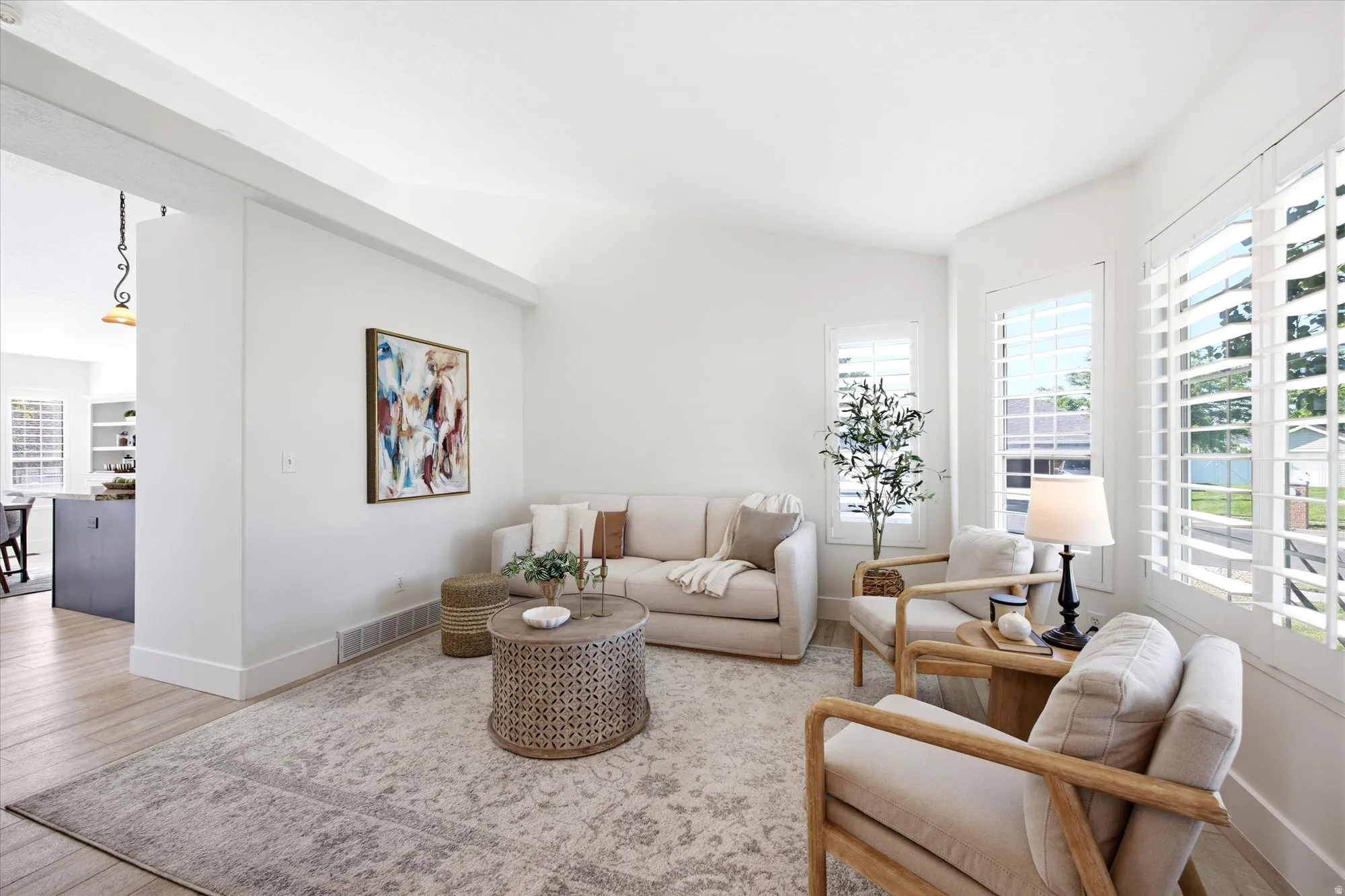 Bright living area featuring white walls, vaulted ceilings, and wood-finish flooring