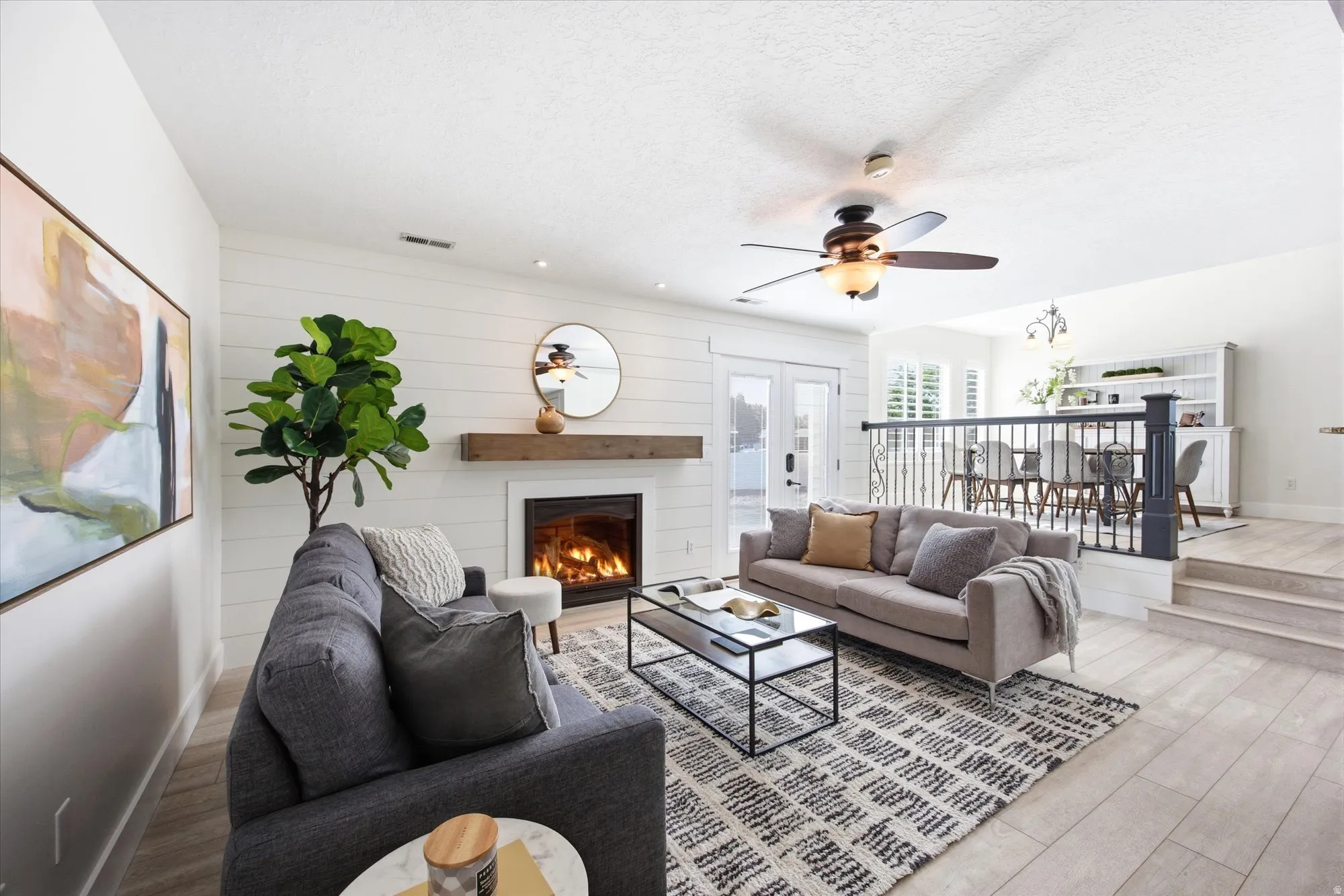 Living area featuring a fireplace with a wood mantel, shiplap accent wall, and a ceiling fan