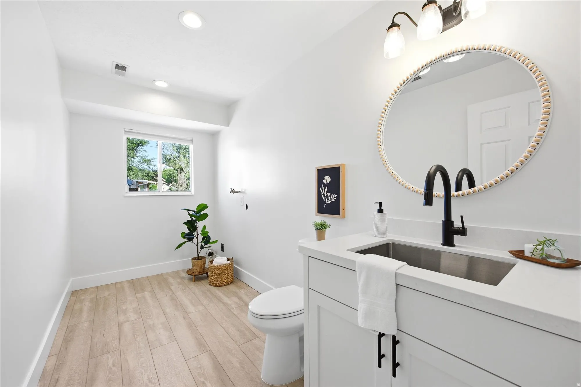 Contemporary bathroom featuring a white vanity with a stainless steel undermount sink, a matte black faucet, and a round decorative mirror