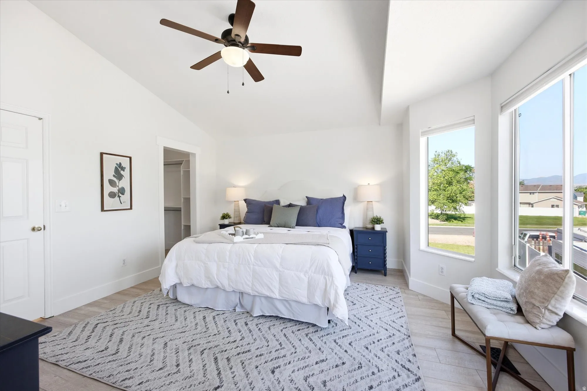 Spacious room featuring vaulted ceilings, wood-finish flooring, a contemporary ceiling fan, and large windows providing ample natural light