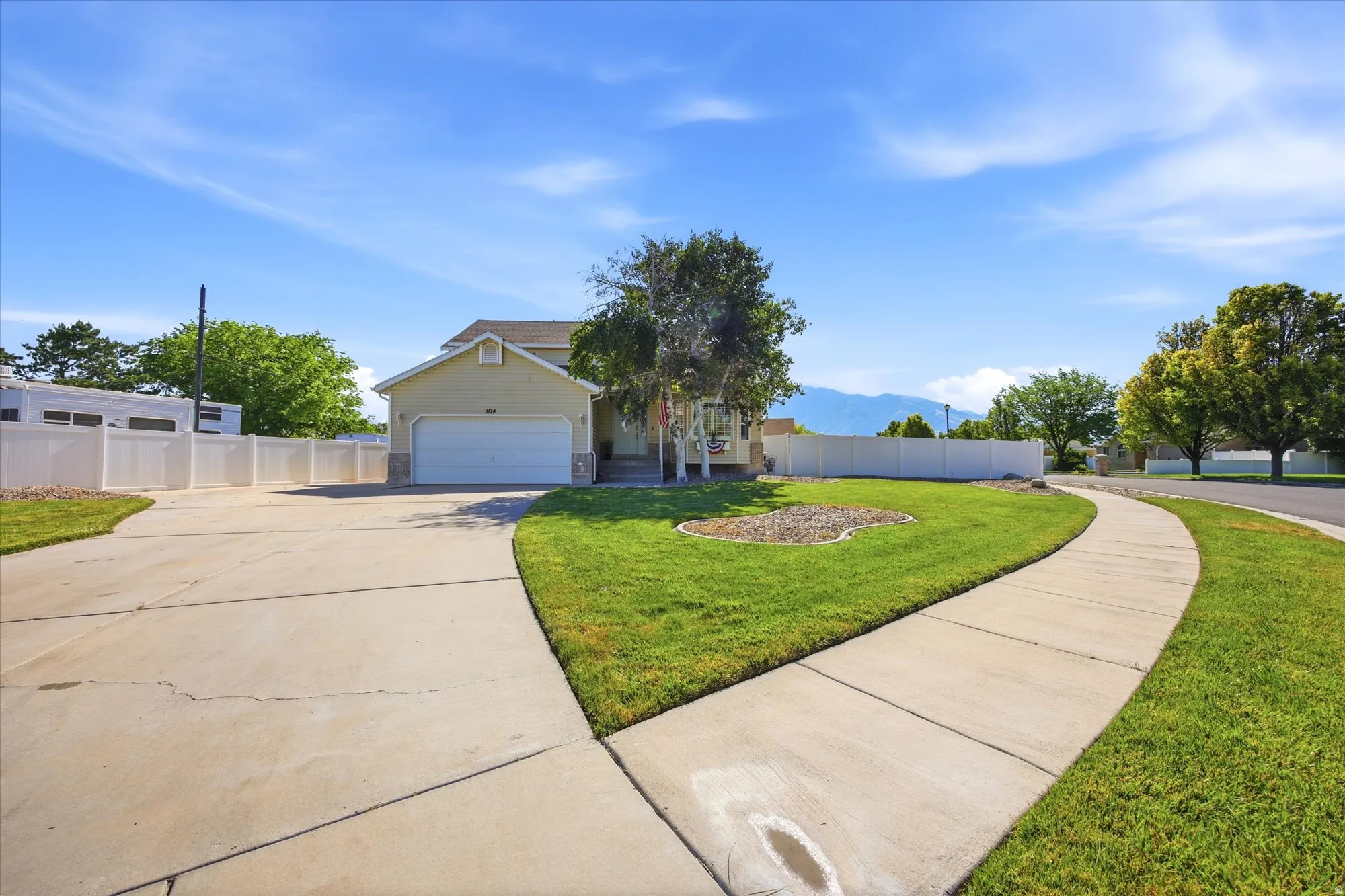 Cream-colored exterior featuring a two-car garage, stone veneer accents, and a front porch