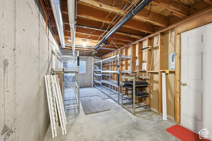 Unfinished basement offering exposed concrete walls, concrete flooring, exposed ceiling joists, and a paneled white door