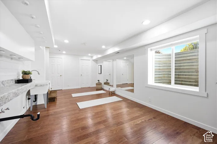 Finished basement space featuring wood-finish flooring, recessed lighting, and a utility sink with a stone-finish countertop