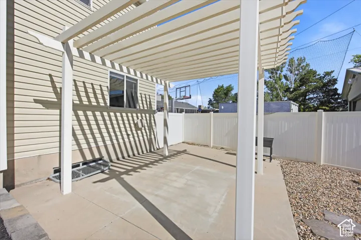 Rear patio featuring a pergola, concrete surface, and white privacy fencing
