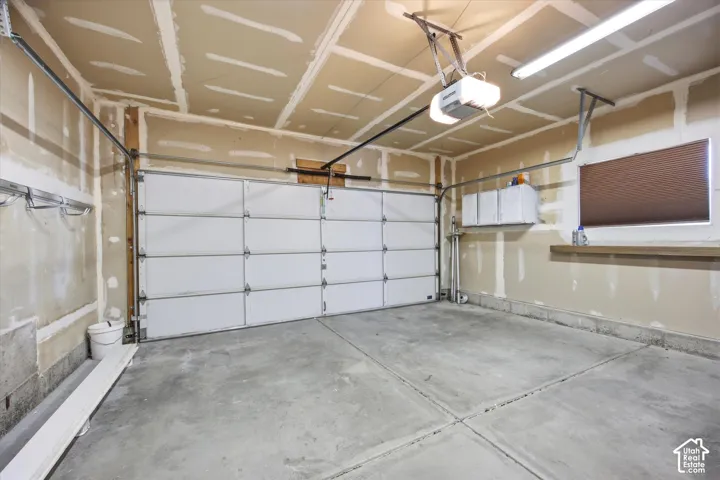 Concrete flooring garage featuring a sectional overhead door with an automatic opener, a window with a mounted blind, and built-in overhead fluorescent lighting