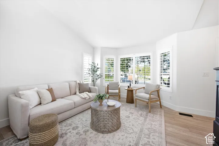 Vaulted ceiling living area featuring a bay window with plantation shutters, wood-finish flooring, and a fireplace with a dark mantel