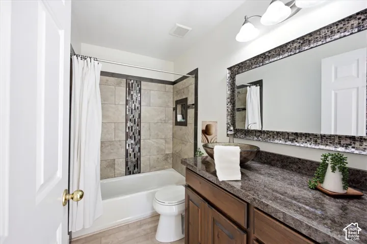 Bathroom featuring a tub/shower combination with mosaic tile accent, dark wood-finish vanity with stone-finish countertop, and vessel sink