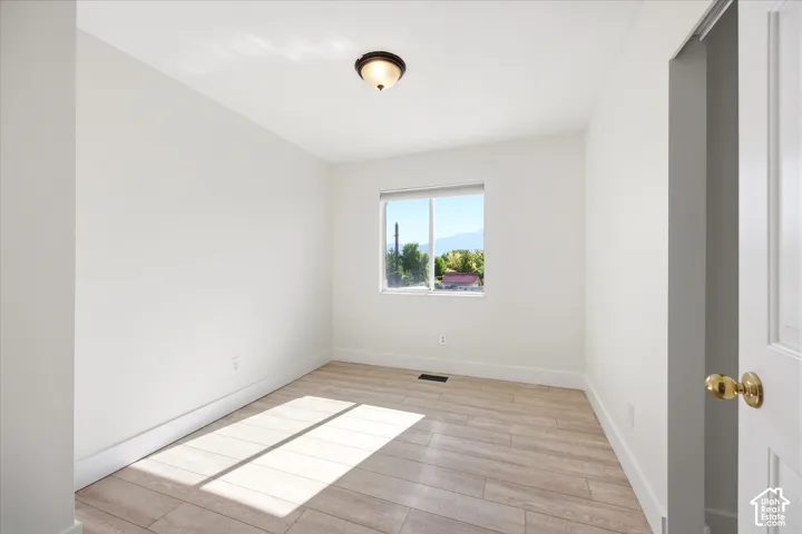 Neutral toned room featuring a single window, a ceiling-mounted light fixture, wood-finish flooring, and white trim
