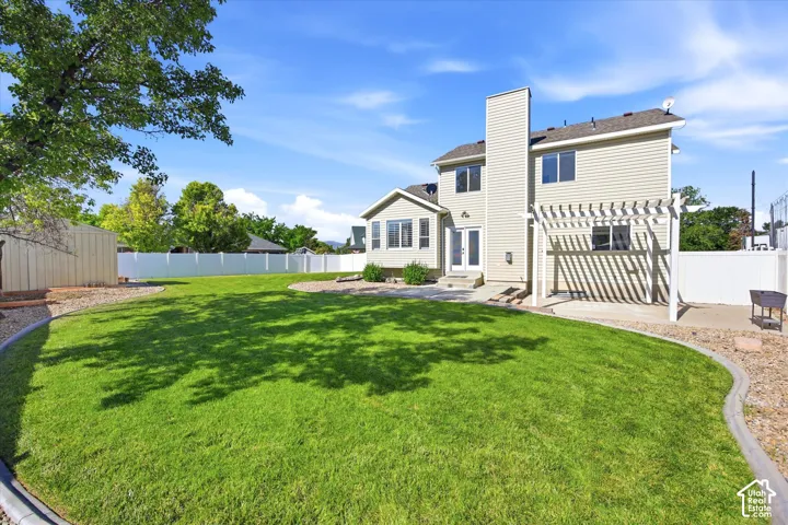 Expansive fenced backyard featuring a substantial lawn, paved patio with a pergola, and a sunroom with exterior access