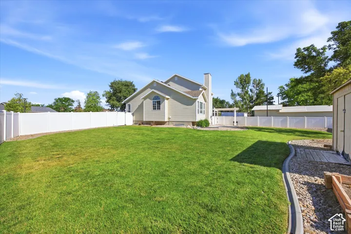 Expansive backyard featuring a lush lawn, white vinyl fencing, a gravel pathway with concrete edging, and a separate storage shed
