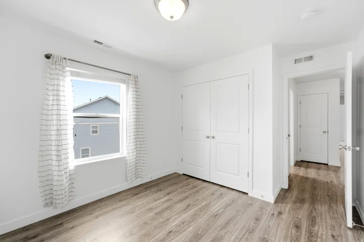 Bright room featuring wood-finish flooring, a double-door closet, a window with a sheer curtain treatment, and white trim throughout