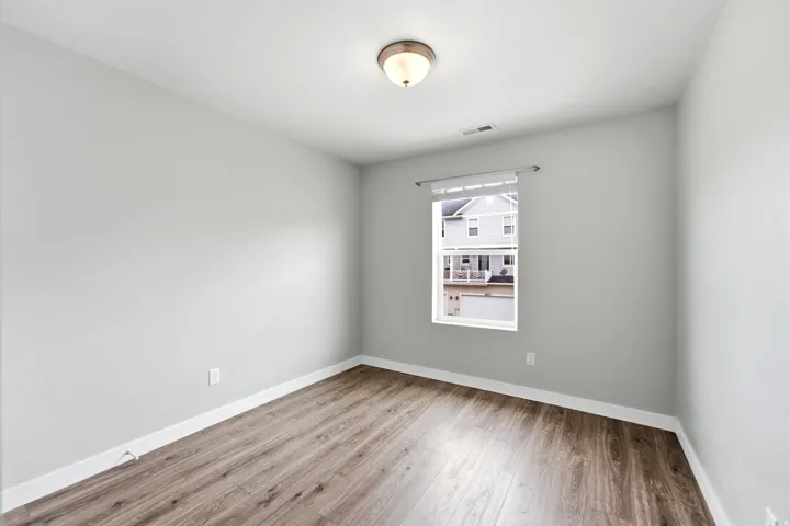 Room featuring wood-finish flooring, light grey painted walls, white baseboards, a single window with a white blind, and a flush-mount ceiling light fixture