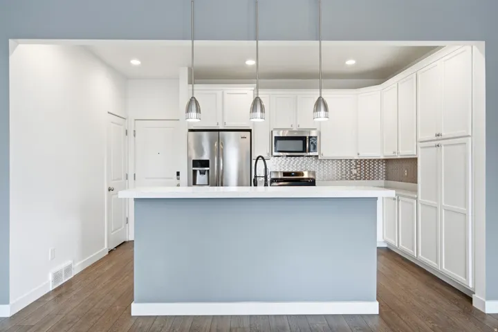 Kitchen featuring white shaker cabinetry, stainless steel appliances, a white countertop island with pendant lighting, and wood-finish flooring