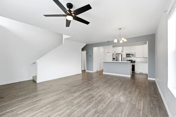 Open-concept living area featuring wood-finish flooring, a modern black ceiling fan, and a staircase with a white handrail