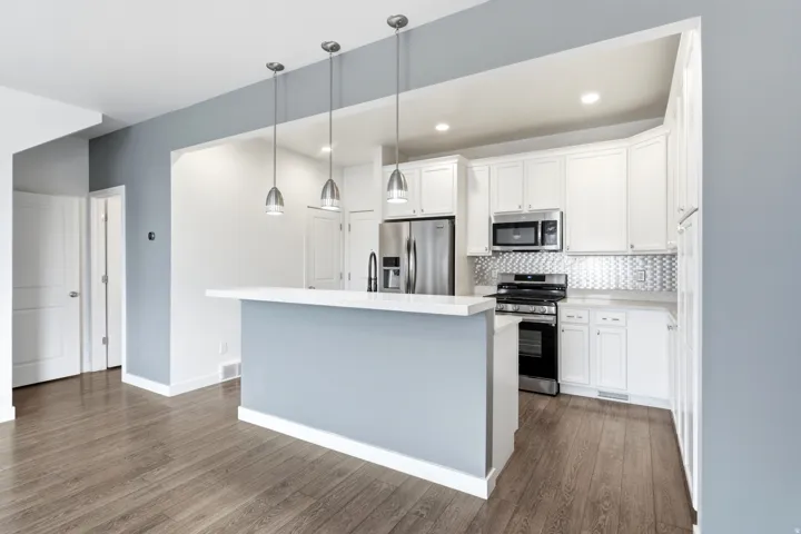 Modern kitchen featuring white cabinetry, stainless steel appliances, a tile backsplash, wood-finish flooring, and a breakfast bar with pendant lighting
