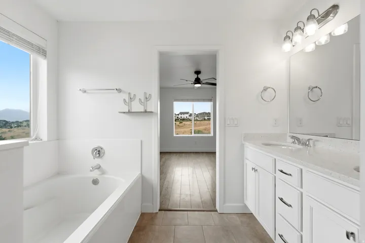 Bathroom featuring a built-in tub, dual sink vanity with stone countertop, polished chrome fixtures, and a large window