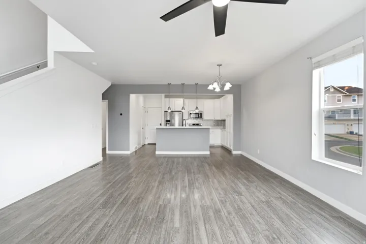 Open-concept living space featuring wood-finish flooring, a contemporary ceiling fan, and a kitchen with white cabinetry, stainless steel appliances, and an island with pendant lighting
