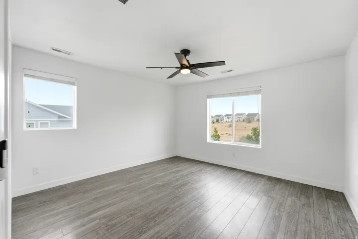 Spacious room featuring wood-finish flooring, white walls, and a contemporary ceiling fan with integrated lighting