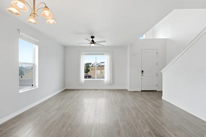 Spacious living area featuring light wood-finish flooring, multiple windows, a ceiling fan, and an elegant chandelier