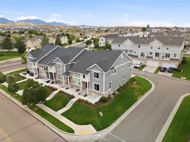 Modern townhome exterior featuring light gray siding, stone accents, dark shingles, and individual front entrances with red doors