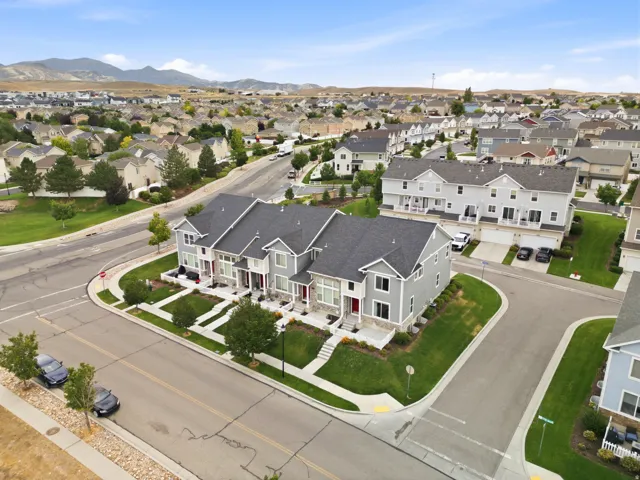Contemporary townhome-style residences featuring gray siding and dark shingle roofs, situated on a corner lot with green lawns