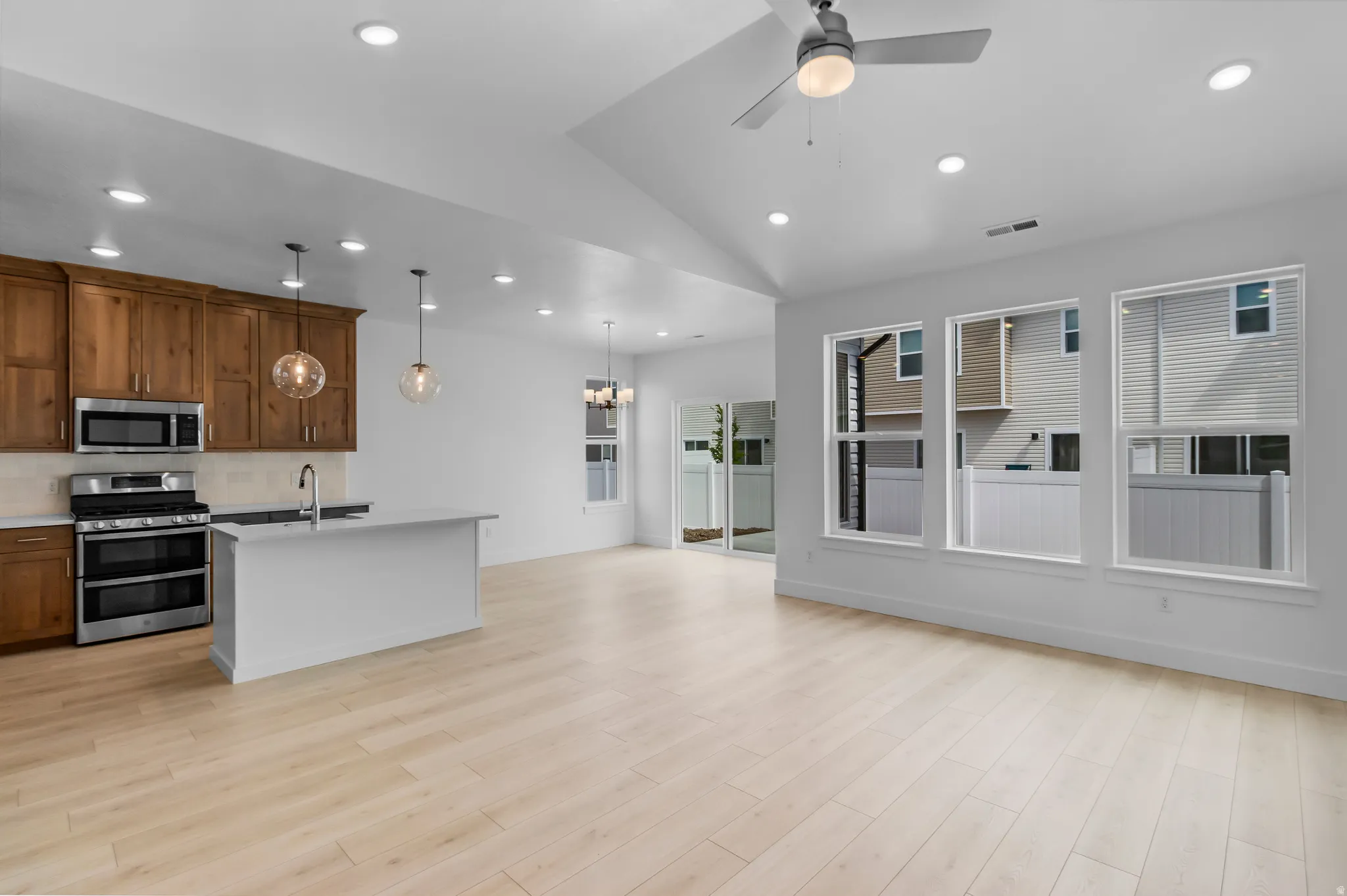 Kitchen and living area featuring light wood-finish flooring, recessed lighting, and a vaulted ceiling with a ceiling fan