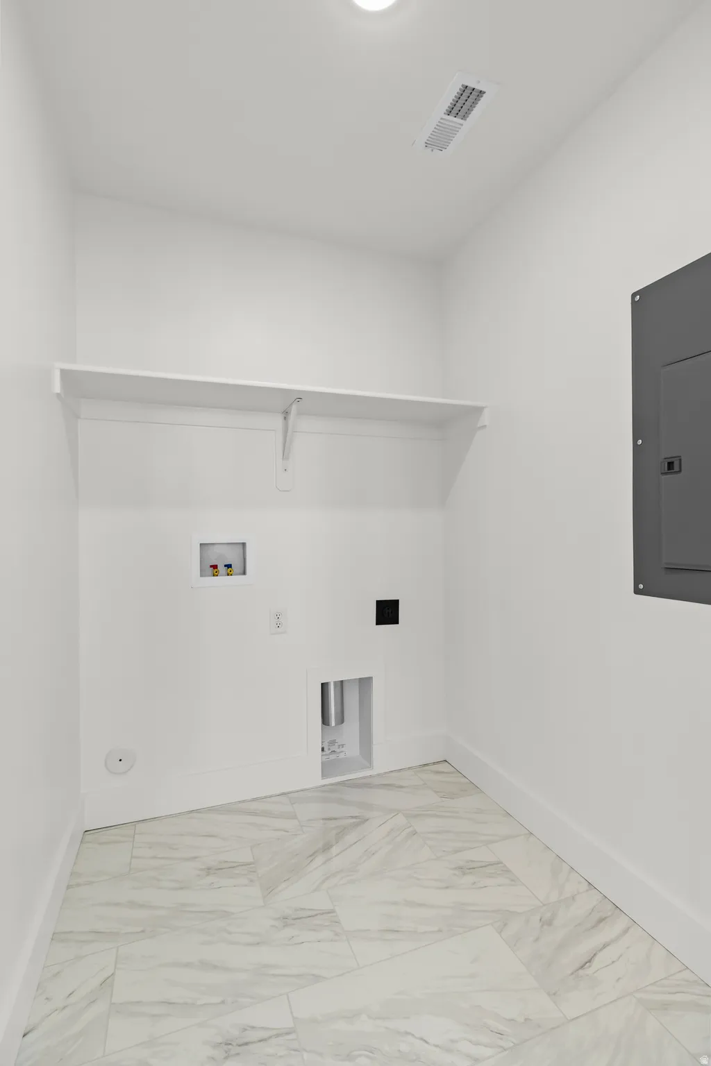 Utility room with white walls, a white storage shelf, and light-toned tile flooring