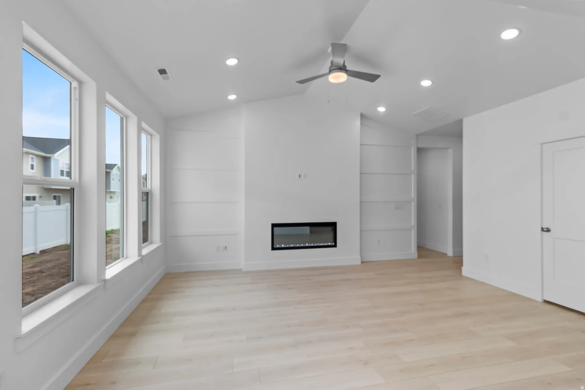 Living area featuring multiple large windows, light wood-finish flooring, recessed lighting, and a modern linear electric fireplace
