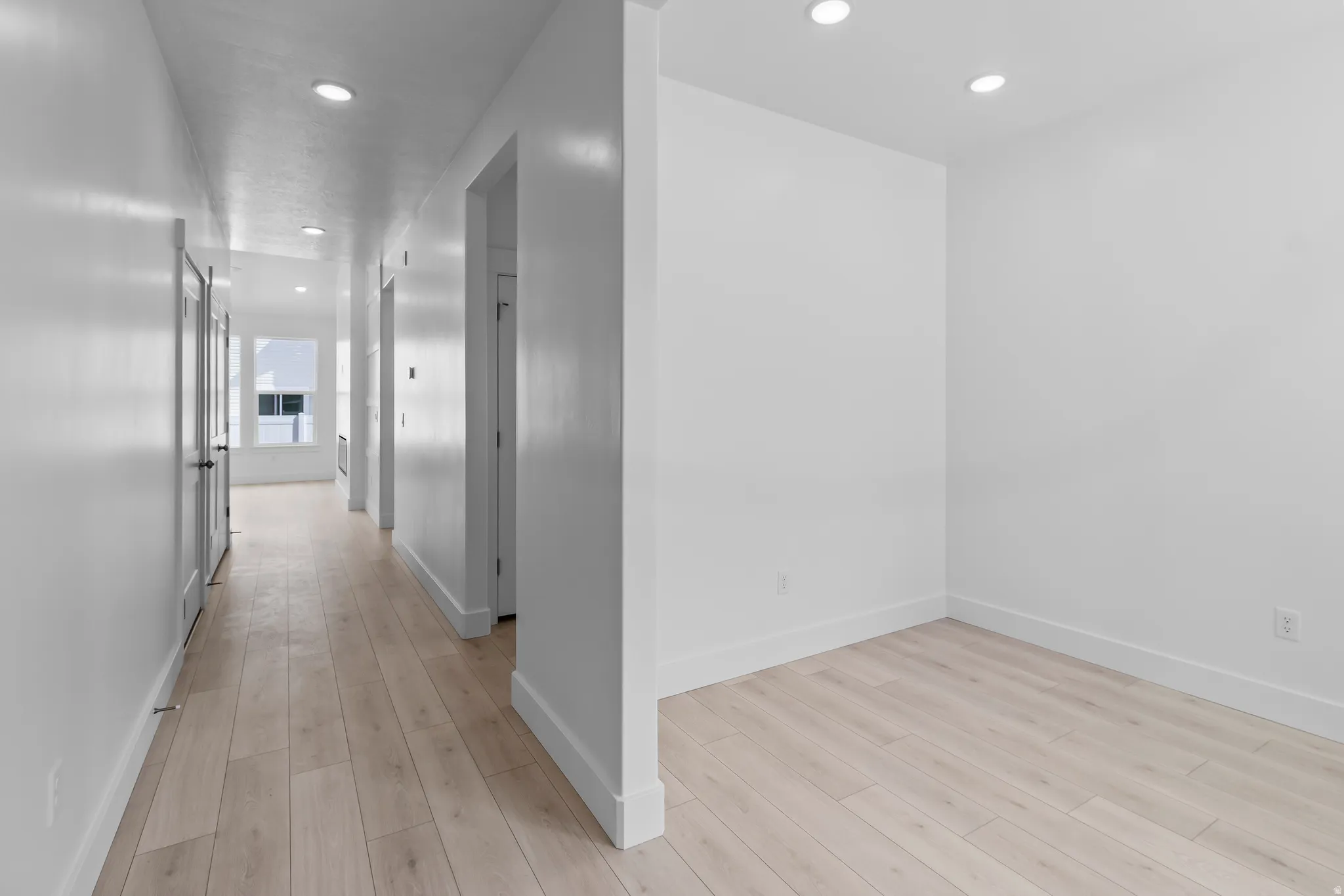 Hallway featuring light wood-finish flooring, recessed ceiling lighting, and white baseboards