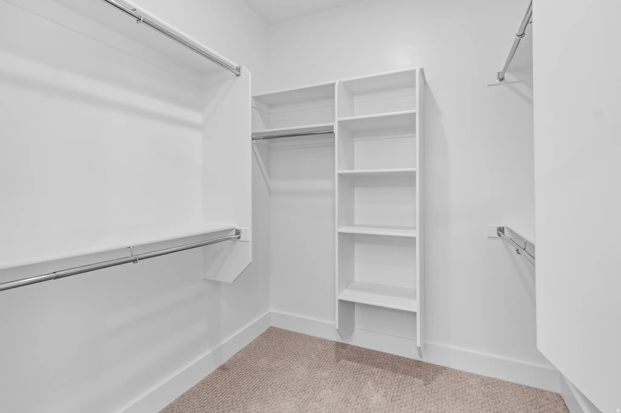 Walk-in closet featuring white built-in shelving, multiple hanging rods, and carpet flooring