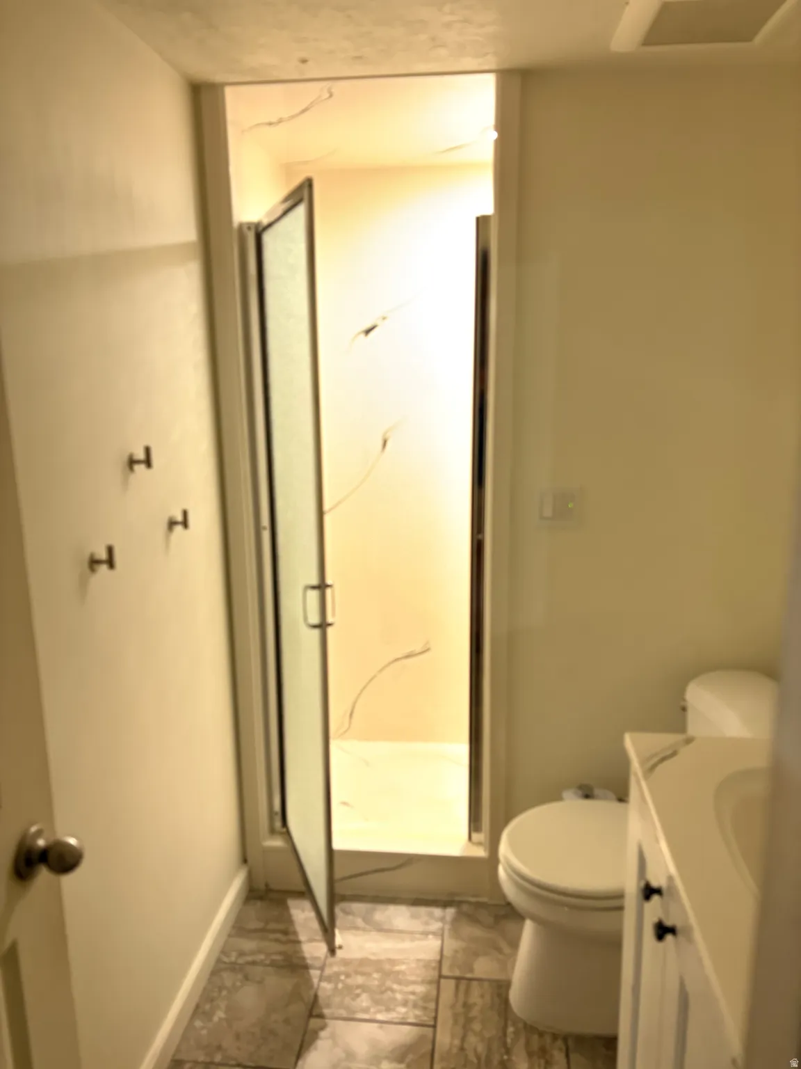 Bathroom featuring a glass-enclosed shower, a white vanity with an integrated sink, dark cabinet hardware, a toilet, and neutral-toned tiled flooring
