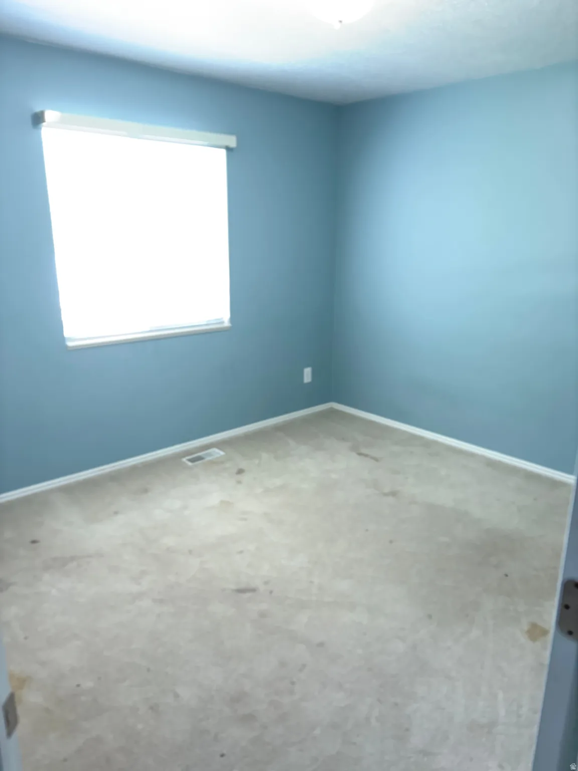 Room featuring light blue walls, white trim, and a single window with a roller shade