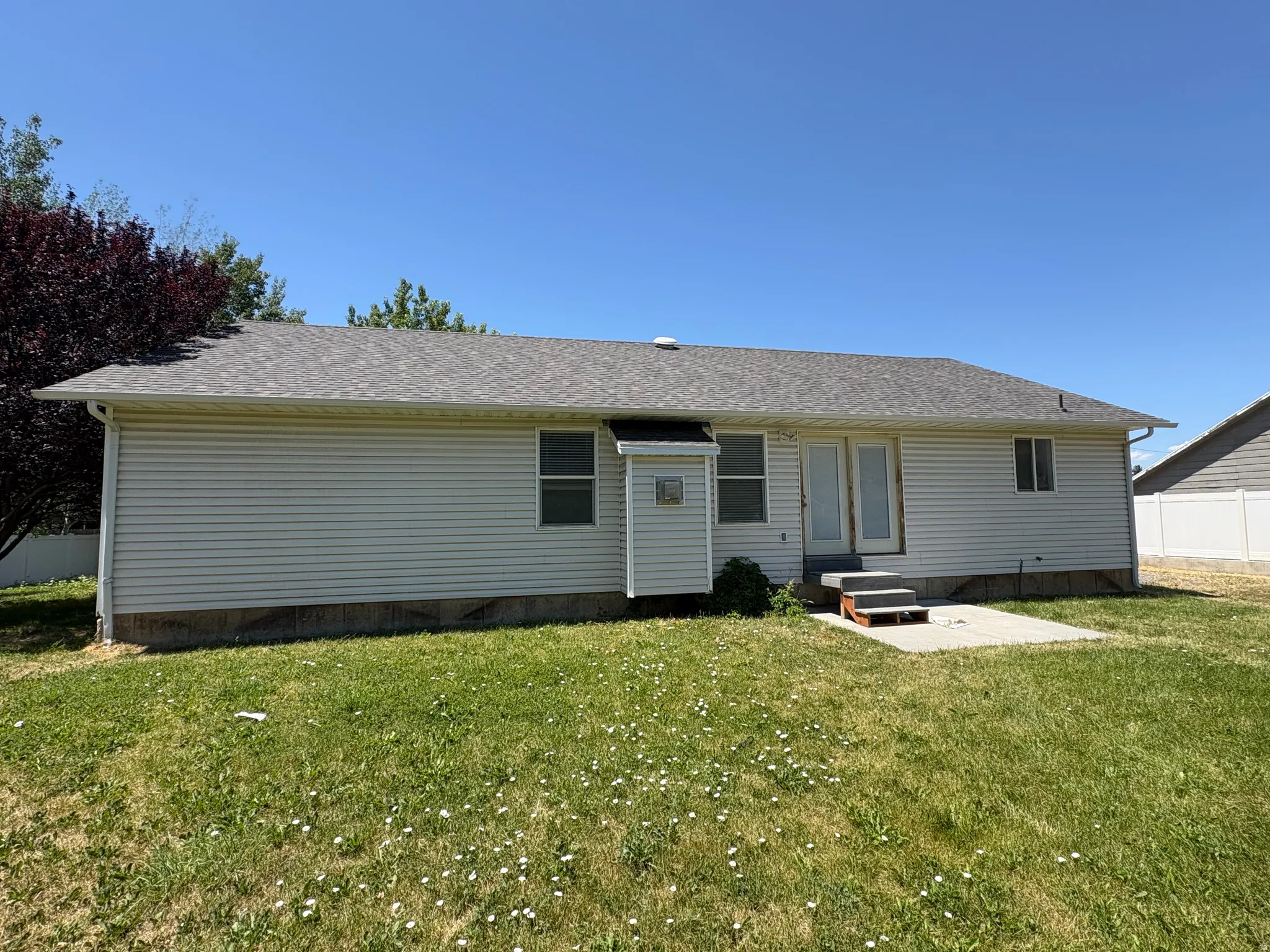 Rear exterior featuring white vinyl siding, a gray shingle roof, a concrete patio, and a double-door entry